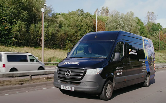 A black Mobility Solutions Mercedes-Benz van providing aftercare support service while driving on a motorway.