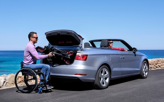 Man in wheelchair putting another wheelchair in car boot