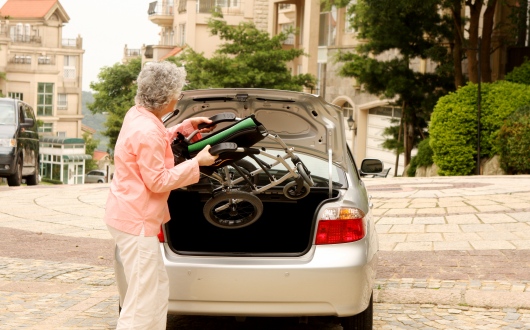 Elderly woman placing wheelchair into car boot