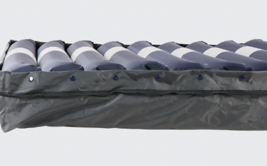 Close-up view of an Opera Flo Auto Air alternating pressure air mattress with blue and white air cells, partially covered by a grey fabric cover with a zip.