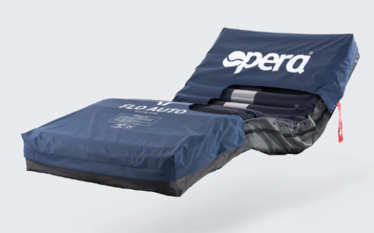 A blue medical air mattress with the brand name Opera Flo Auto Air on the cover, partially elevated and uncovered at one end to show inner support cylinders.