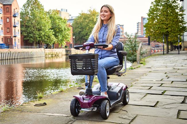Woman using class 2 mobility scooter on pathway.