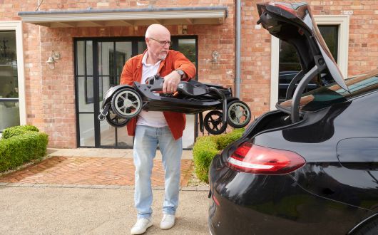 Man lifting folded mobility scooter into a car boot.