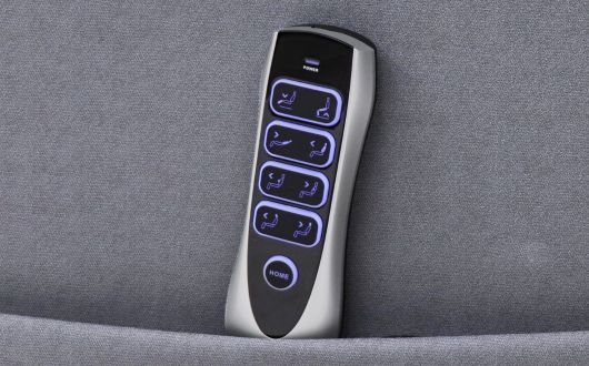 A Dallux Nevis remote control with six illuminated buttons featuring seat adjustment icons, resting upright in a fabric pouch.